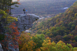 Two hikers on a rocky jag overlooking a wooded valley, autumn colors