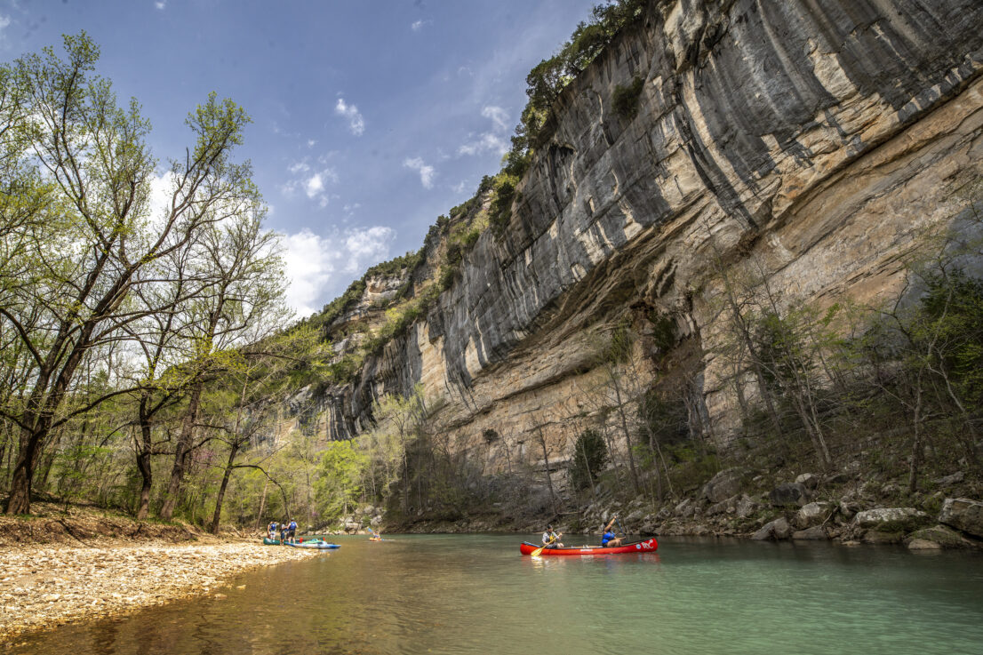 Cliffs overlooking the Buffalo River. People are in a canoe in the middle of the river.