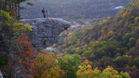 Two hikers on a rocky jag overlooking a wooded valley, autumn colors