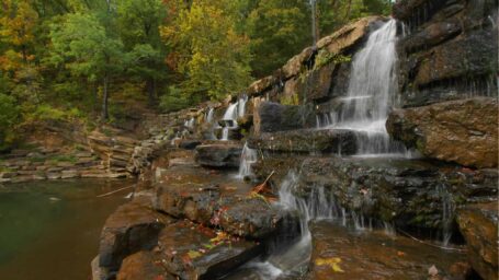 A waterfall cascades over rocks with autumn foliage in the background