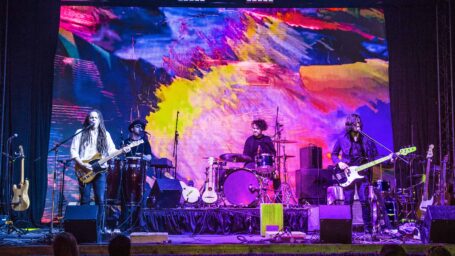 A band plays live on an outdoor stage, in front of a colorful backdrop